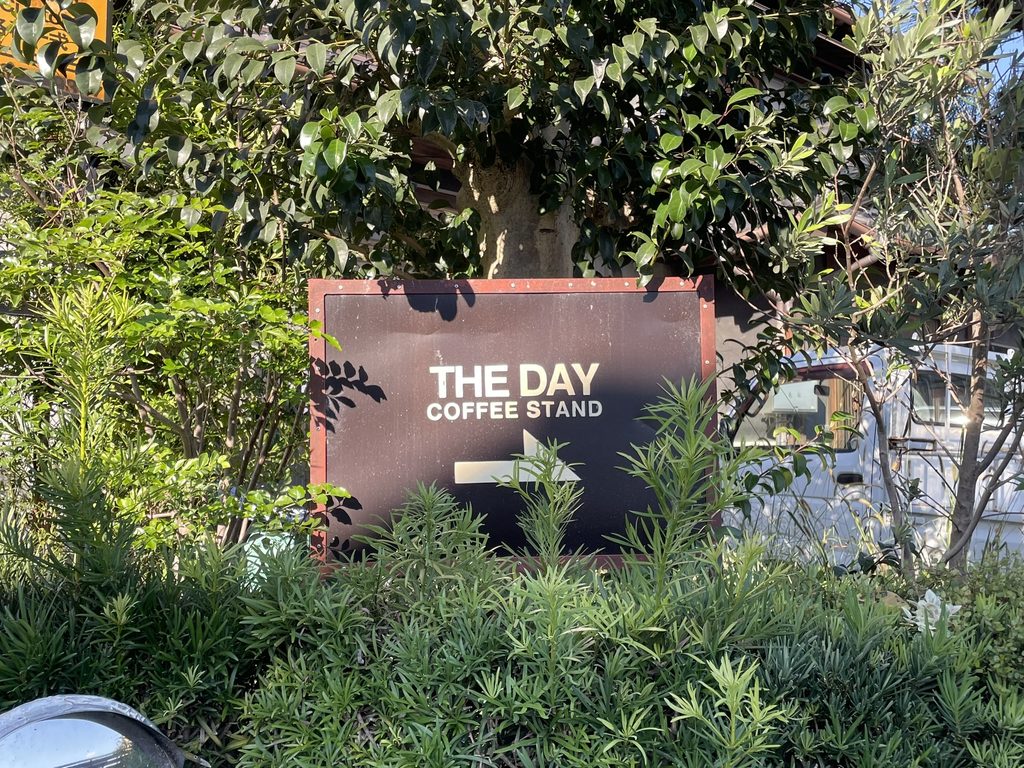 緑に囲まれたTHE DAY COFFEE STANDの看板